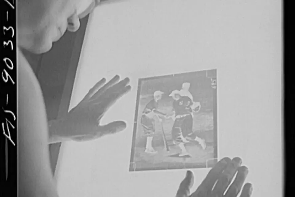Photographie en noir et blanc d'un employé examinant des négatifs photographiques à contre-jour dans un atelier de photogravure